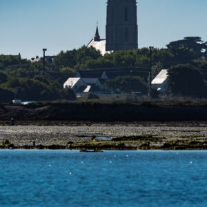 Clocher élancé au-dessus des toits au téléobjectif, de l’autre côté d’un chenal bleu, Le Croisic, Bretagne, France
