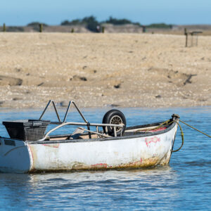 Small white dinghy moored in shallow water off a sandy shore, Le Croisic, Brittany, France
