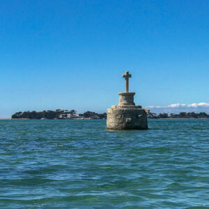 Stone refuge cross standing in the sea at high tide, wooded islet behind, Le Croisic, Brittany, France