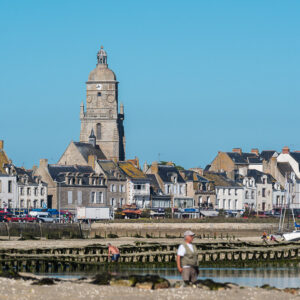 Waterfront houses and domed church tower above quay at low tide, man in foreground, Le Croisic, Brittany, France