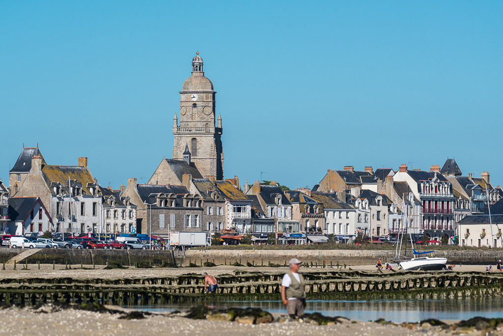 Waterfront houses and domed church tower above quay at low tide, man in foreground, Le Croisic, Brittany, France