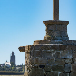 Low-angle stone cross on masonry plinth with distant church tower at left, Le Croisic, Brittany, France