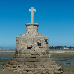 Vertical refuge cross with crumbling masonry base on wet sand under deep blue sky, Le Croisic, Brittany, France