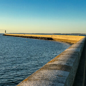 Long stone breakwater curving out to sea toward distant light in warm low light, Le Croisic, Brittany, France