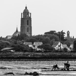 Black-and-white church tower above village with two shellfish gatherers on flats, Le Croisic, Brittany, France