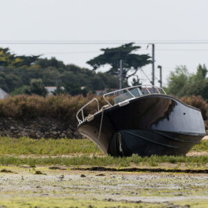 Bateau à moteur sombre échoué sur le pré salé à marée basse, Le Croisic, Bretagne, France