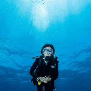 Plongeuse en suspension dans le bleu sous la surface ensoleillée, cadrage vertical, Misool, Raja Ampat, Indonésie