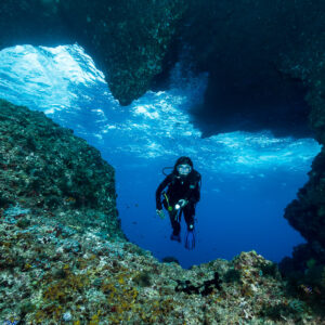 Woman diver framed inside an underwater arch opening, Misool, Raja Ampat, Indonesia