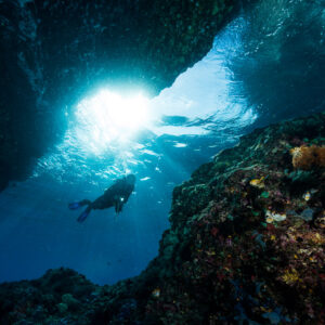 Diver swimming through a sunlit cave opening, seen from inside, Misool, Raja Ampat, Indonesia