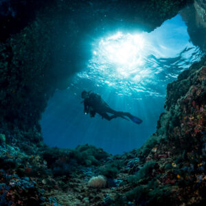 Diver backlit by sunbeams in a cave arch, Misool, Raja Ampat, Indonesia