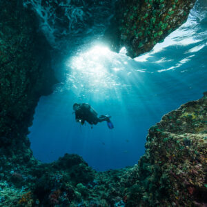 Silhouette de plongeuse dans une large ouverture de grotte traversée de rayons, Misool, Raja Ampat, Indonésie