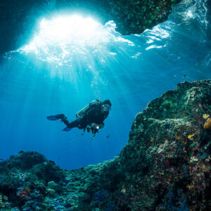 Woman diver in a sunlit cave entrance with light rays, Misool, Raja Ampat, Indonesia
