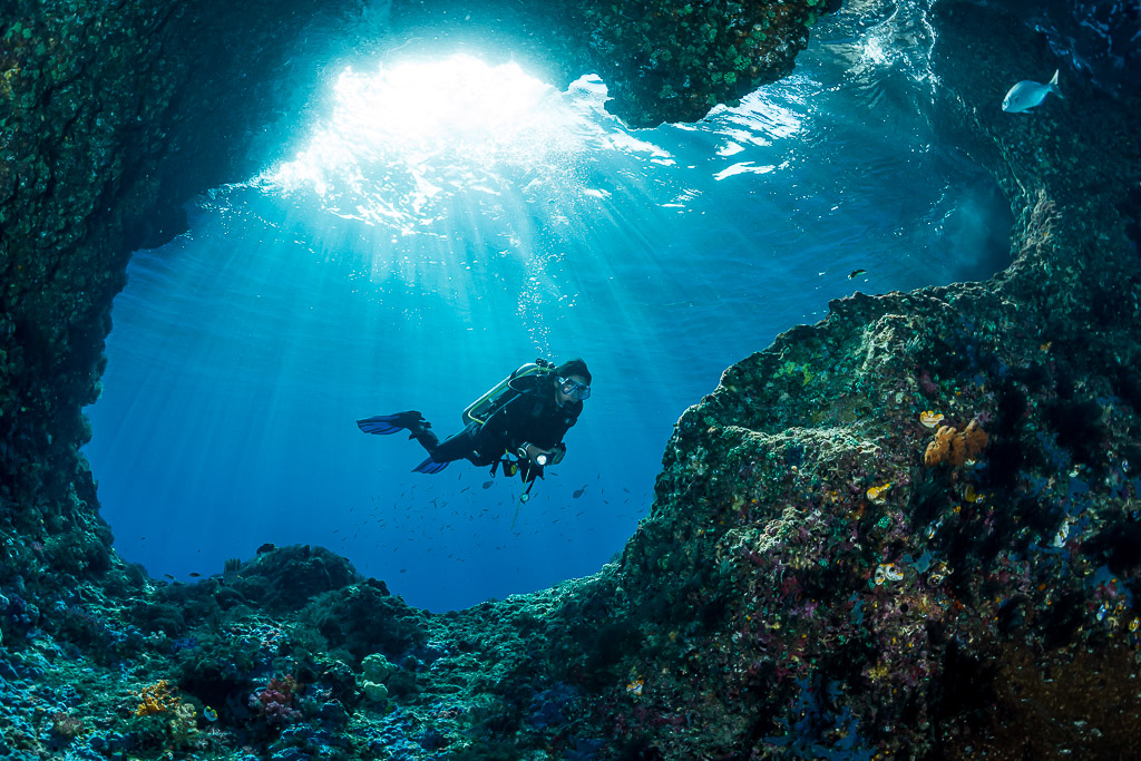 Woman diver in a sunlit cave entrance with light rays, Misool, Raja Ampat, Indonesia