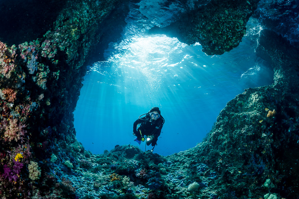 Woman diver approaching the camera through a cave entrance, Misool, Raja Ampat, Indonesia