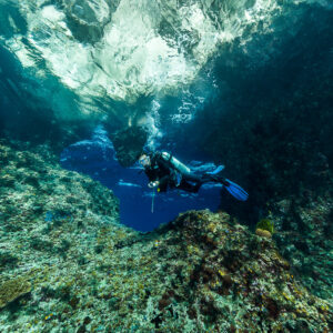Diver exploring a cave mouth beneath a mirrored surface, Misool, Raja Ampat, Indonesia