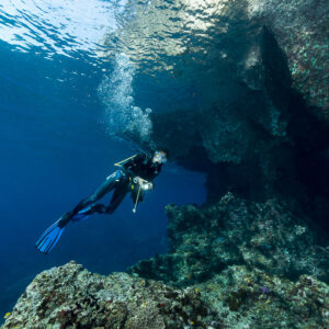 Diver ascending past a cave entrance trailing bubbles, Misool, Raja Ampat, Indonesia