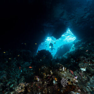 Minuscule plongeuse dans une lointaine fenêtre de grotte, premier plan sombre, Misool, Raja Ampat, Indonésie