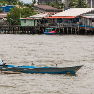Man sitting in a blue wooden boat in front of stilt houses, Misool, Raja Ampat, Indonesia