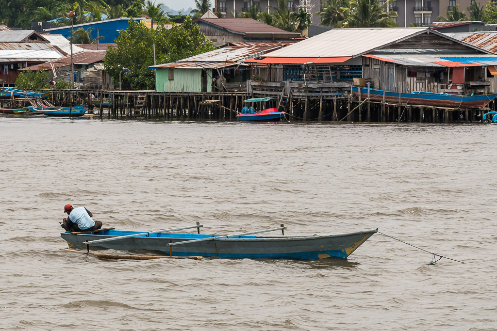 Man sitting in a blue wooden boat in front of stilt houses, Misool, Raja Ampat, Indonesia