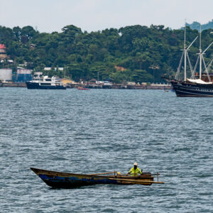 Fisherman in a wooden canoe with a schooner in the background, Misool, Raja Ampat, Indonesia