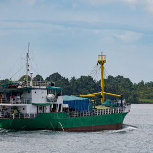 Green-hulled cargo ship with yellow crane under way, Misool, Raja Ampat, Indonesia