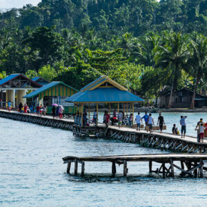 Villageois marchant sur une longue jetée en bois vers des pavillons à toits bleus, Misool, Raja Ampat, Indonésie