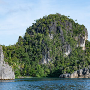 Rounded karst islet with grey cliffs and a rock in foreground, Misool, Raja Ampat, Indonesia