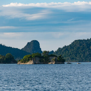 Low wooded islet in front of forested hills and a pointed peak, Misool, Raja Ampat, Indonesia
