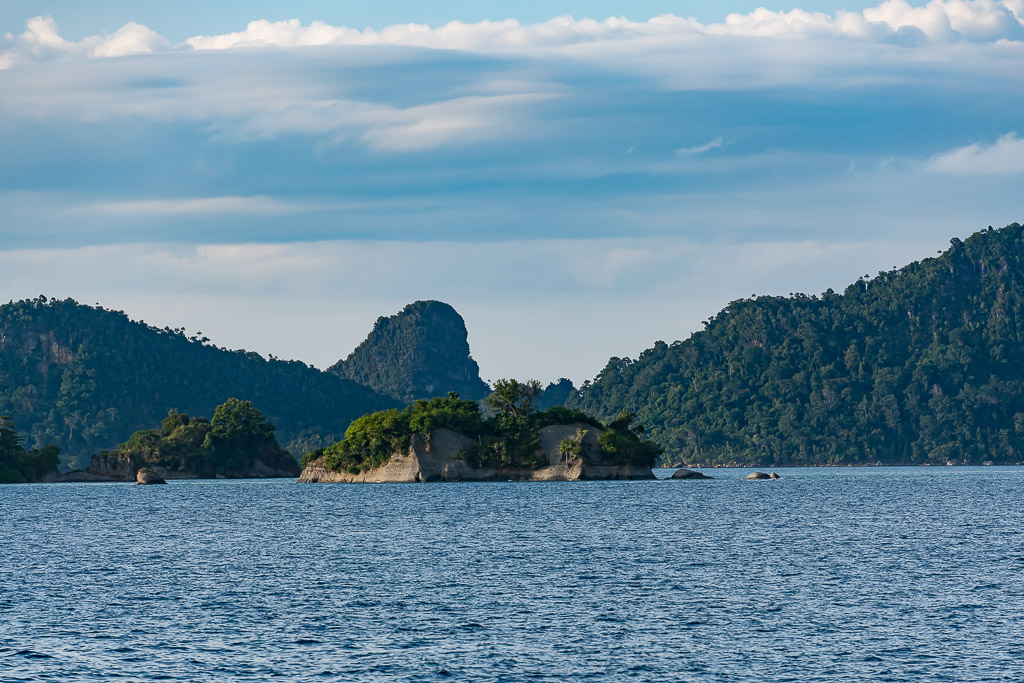 Low wooded islet in front of forested hills and a pointed peak, Misool, Raja Ampat, Indonesia