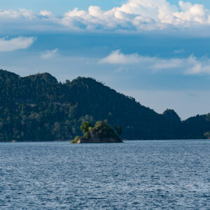 Tiny rocky islet against dark forested mountains, Misool, Raja Ampat, Indonesia