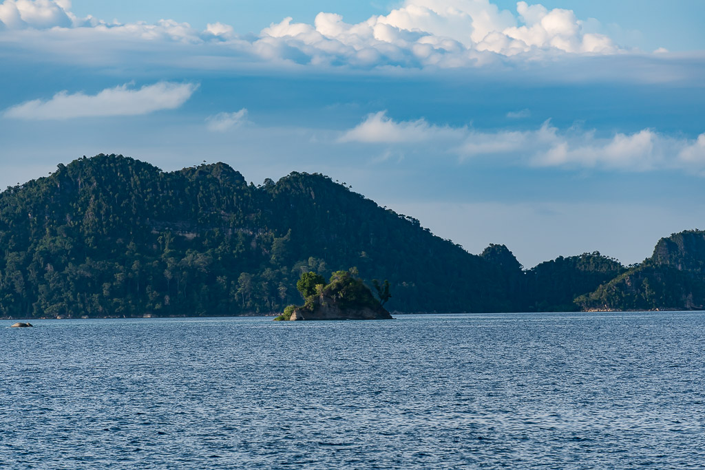 Tiny rocky islet against dark forested mountains, Misool, Raja Ampat, Indonesia