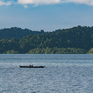 Fishermen in a single canoe below forested hills, Misool, Raja Ampat, Indonesia