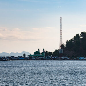 Village sur pilotis avec coupole verte de mosquée et antenne télécom, Misool, Raja Ampat, Indonésie