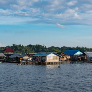 Row of wooden stilt houses with a red roof in late-afternoon light, Misool, Raja Ampat, Indonesia