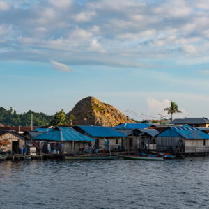 Stilt houses with blue tin roofs below a bare rocky hill, Misool, Raja Ampat, Indonesia