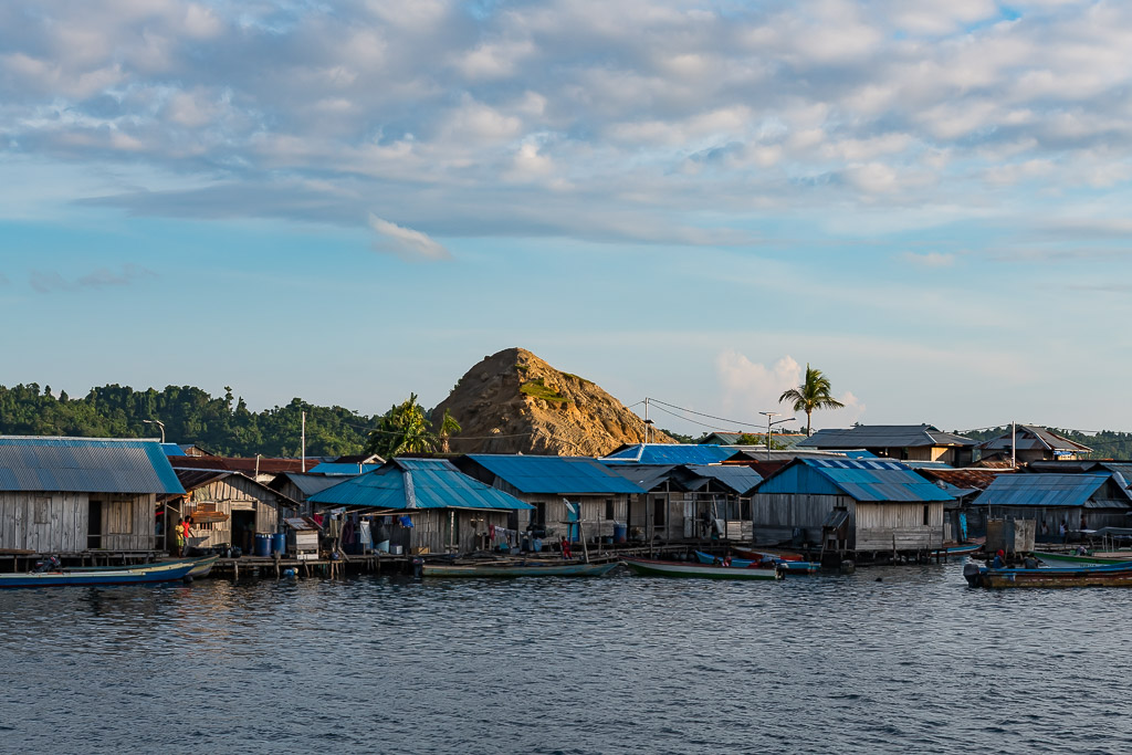 Stilt houses with blue tin roofs below a bare rocky hill, Misool, Raja Ampat, Indonesia