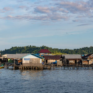 Stilt houses with small green boats moored under pink clouds, Misool, Raja Ampat, Indonesia