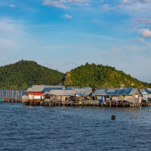 Vue large du village sur pilotis sous des collines vertes et une eau calme, Misool, Raja Ampat, Indonésie