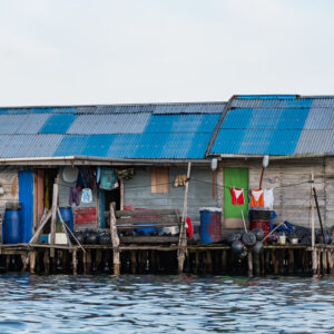 Weathered wooden stilt house with blue tin roof and hanging laundry, Misool, Raja Ampat, Indonesia