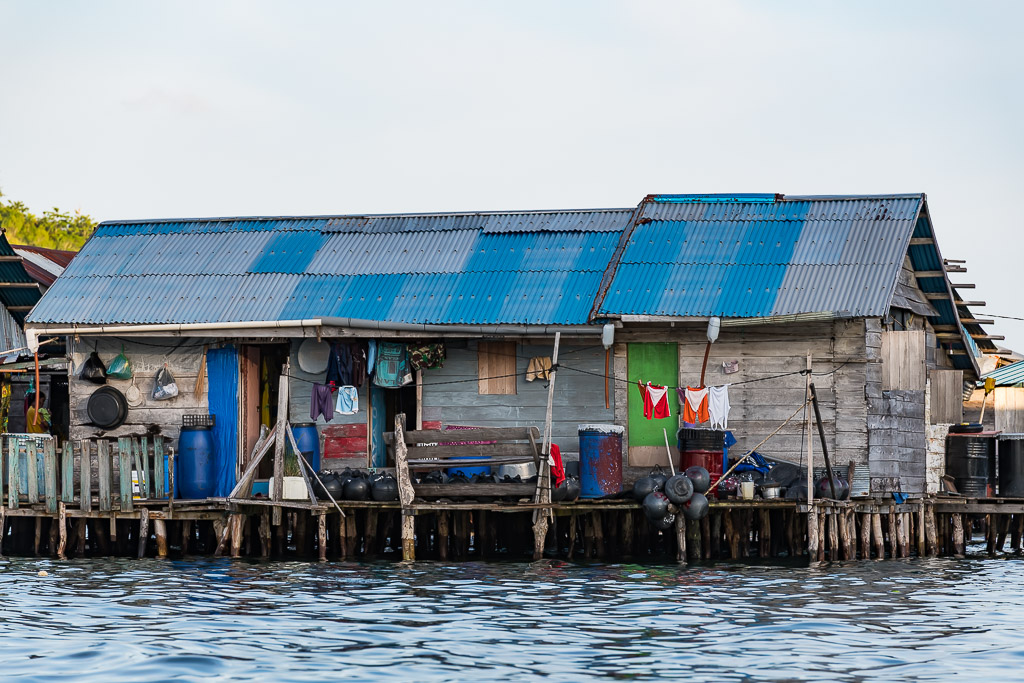 Weathered wooden stilt house with blue tin roof and hanging laundry, Misool, Raja Ampat, Indonesia
