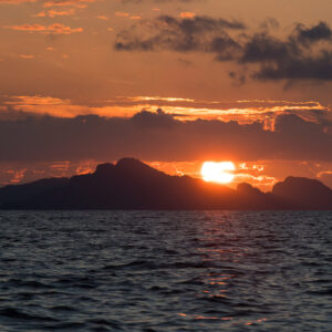Sun setting behind a mountainous island silhouette, orange sky, Misool, Raja Ampat, Indonesia