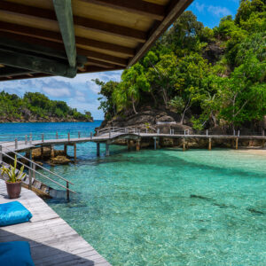 Terrasse d’hôtel avec pouf bleu dominant un lagon turquoise et un ponton, Misool, Raja Ampat, Indonésie
