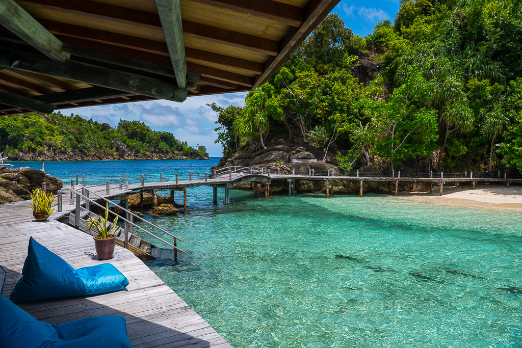 Terrasse d’hôtel avec pouf bleu dominant un lagon turquoise et un ponton, Misool, Raja Ampat, Indonésie