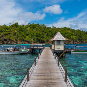 Central perspective of a wooden jetty leading to a hut and dive boats, Misool, Raja Ampat, Indonesia