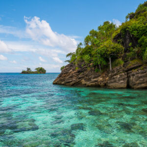 Rocky jungle islet over a turquoise reef flat, small islet beyond, Misool, Raja Ampat, Indonesia