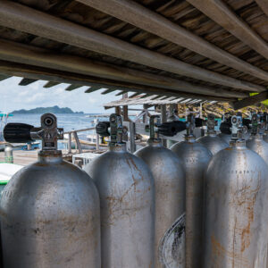 Row of aluminium scuba tanks under a jetty shelter, boat behind, Misool, Raja Ampat, Indonesia