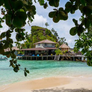 Bâtiments d’hôtel vus depuis la plage, encadrés par des feuillages, Misool, Raja Ampat, Indonésie