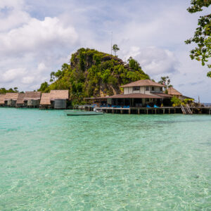 Bungalows en chaume sur pilotis au pied d’une falaise verdoyante, Misool, Raja Ampat, Indonésie