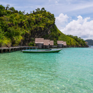 Villas sur pilotis et pirogue à moteur amarrée sous une falaise couverte de jungle, Misool, Raja Ampat, Indonésie