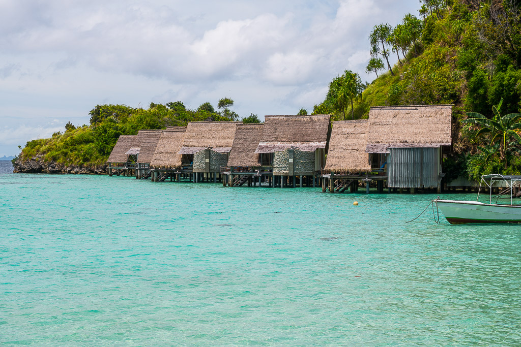 Row of thatched overwater bungalows along a green hillside, Misool, Raja Ampat, Indonesia
